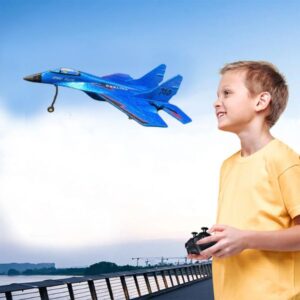 Un joven sonriente con un control remoto operando alegremente un modelo de avión volador contra un cielo azul claro.