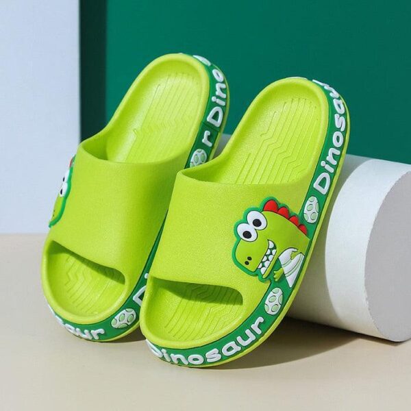 Un par de zapatillas infantiles de color verde brillante con un bonito motivo de dinosaurio, sobre un fondo verde y beige.