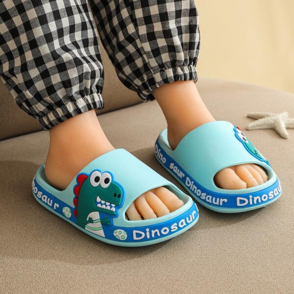 Pies de niño con lindas pantuflas azules con temática de dinosaurios.