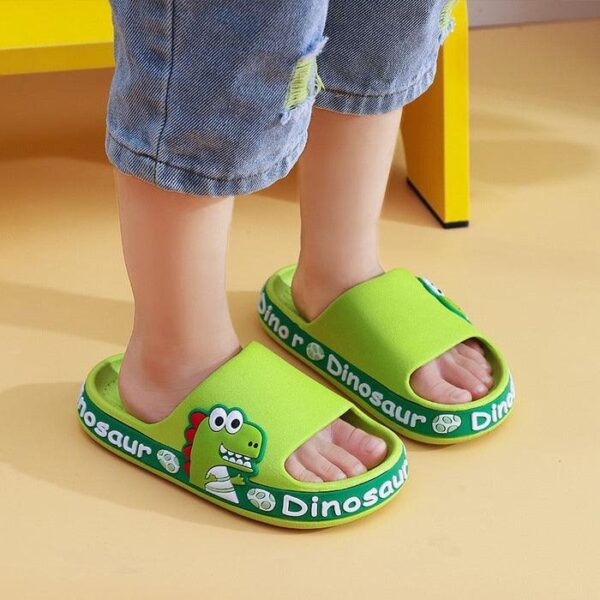 Pies de niño pequeño con sandalias deslizantes de color verde brillante con temática de dinosaurios sobre un fondo amarillo.