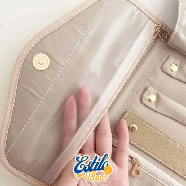 A partially open pink pencil case showing a transparent compartment with a hand inside it. The case has gold button snaps, a zipper pocket, and pen loops. The logo "Estilo Ideal" with a balloon lightbulb icon is at the bottom center of the image.